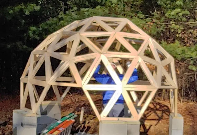 Wooden geodesic dome structure under construction with person inside wearing blue shirt