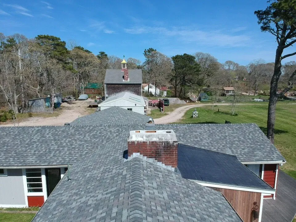Rooftop view of a rural campus with gray buildings, a driveway, trees, and open green grounds under a blue sky