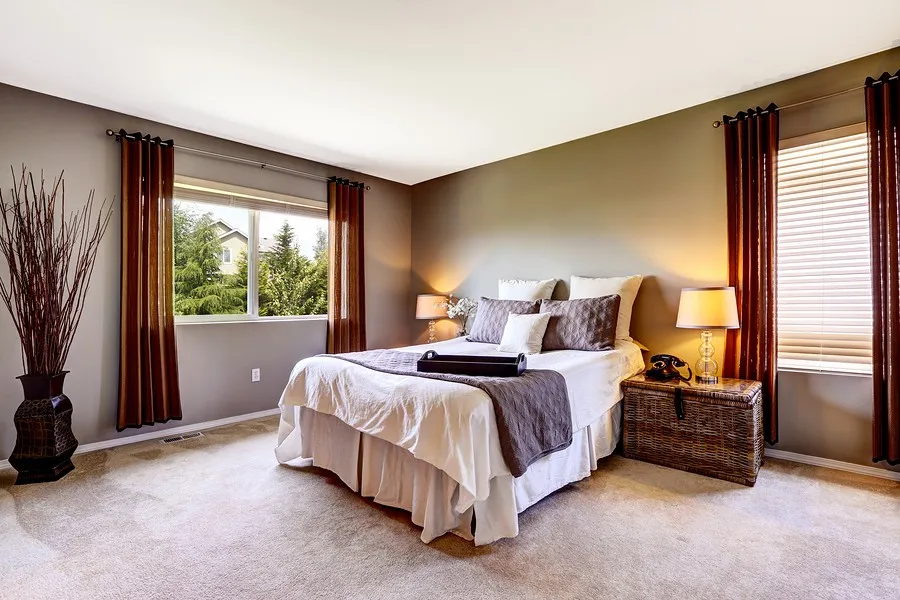 Clean bedroom with made bed, bedside lamps, and windows with curtains in a tidy home interior