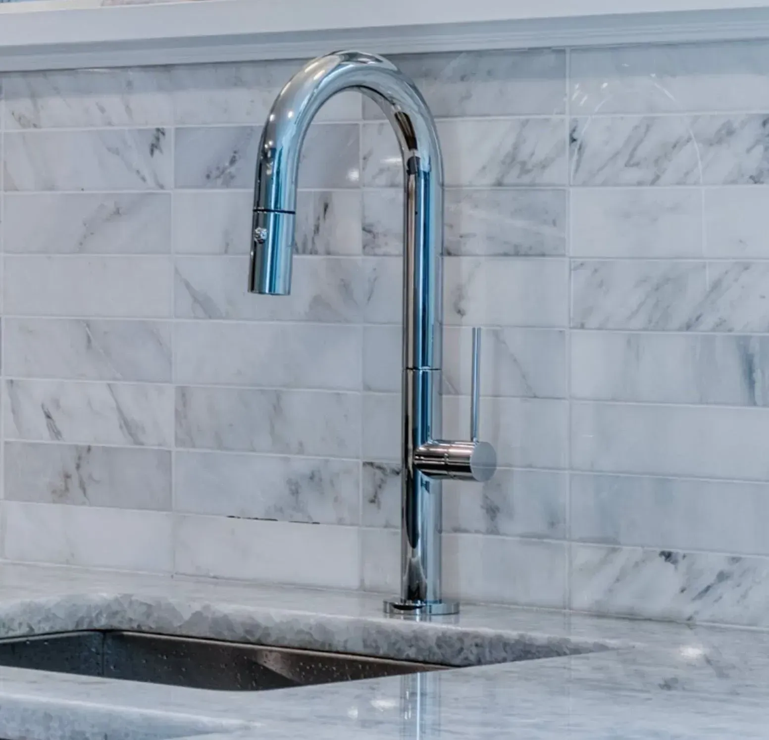 Chrome gooseneck kitchen faucet over a marble countertop and tiled backsplash
