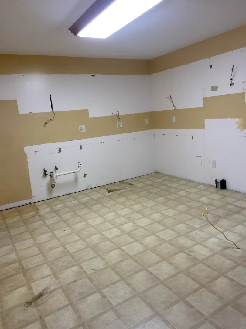 Gutted kitchen with old vinyl tile floor and walls stripped back to studs before remodel