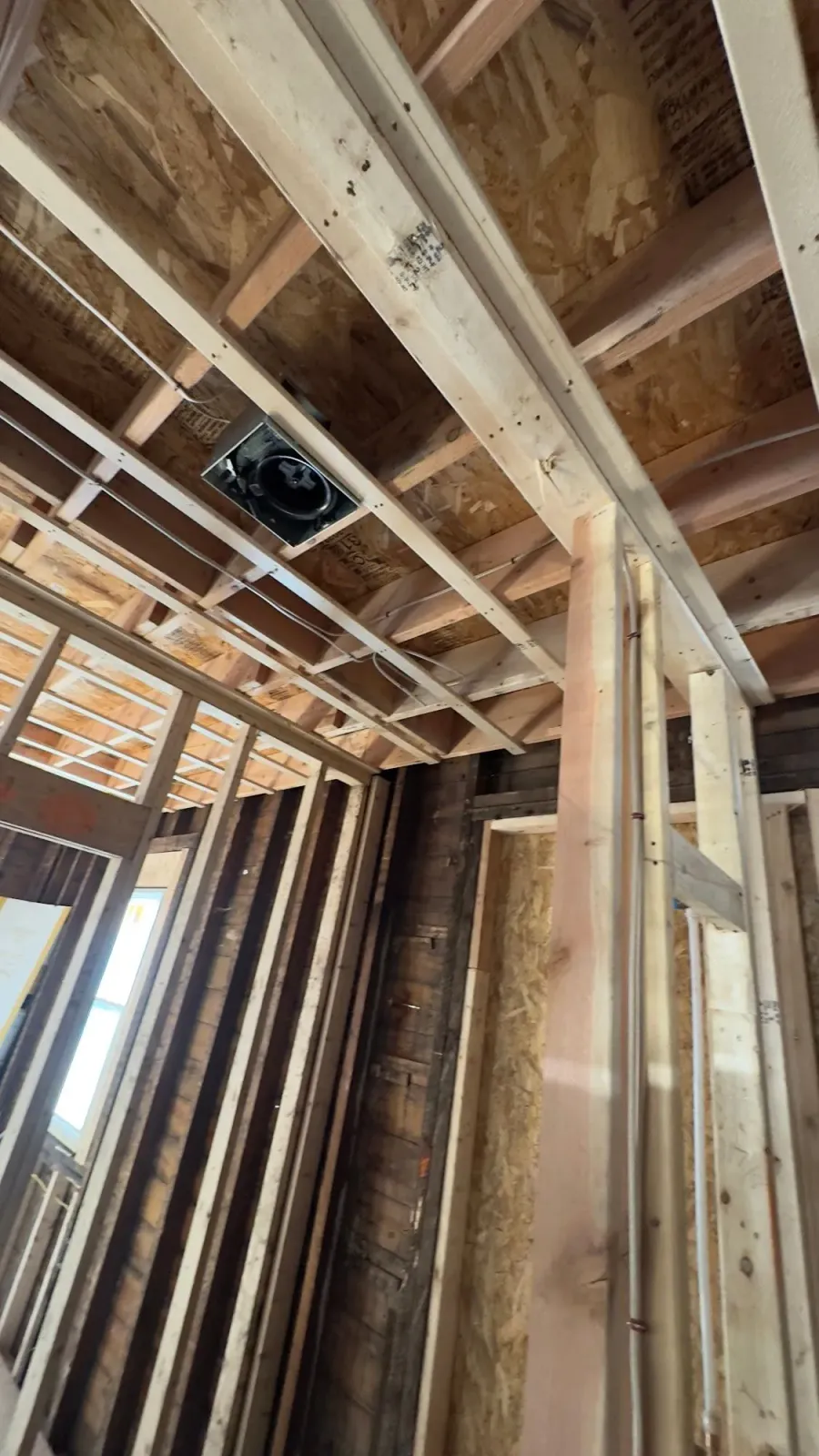 Interior view of a building under construction, showing framing, ceiling beams, and a vent. Wooden structure.