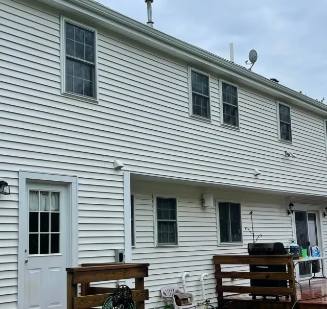 A two-story white house exterior with vinyl siding, several windows, a white door, and a wooden deck.