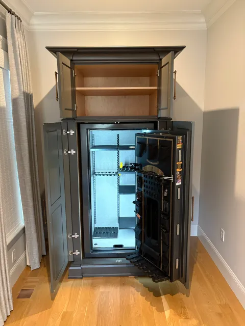 Open gun safe with empty shelves inside, located in a light-colored room with hardwood floors and beige walls.