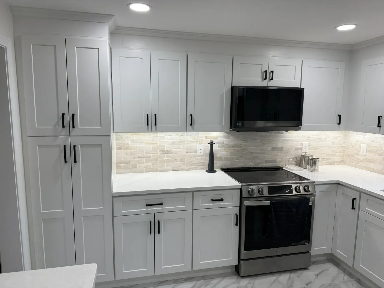 Close-up of white shaker cabinets with black hardware and a natural stone tile backsplash in a Framingham kitchen.