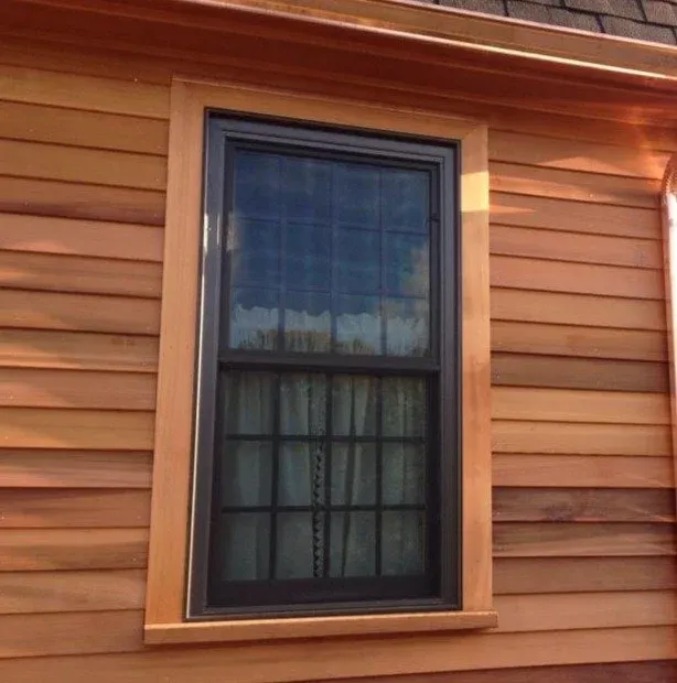 A close-up of a black-framed window set in a brown wooden house exterior with horizontal siding.