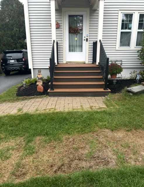 Front porch with dark stairs, white door, and black railings leading to a gray house.