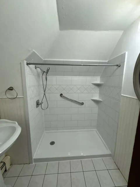 A white walk-in shower with a white base, silver fixtures, and built-in shelves