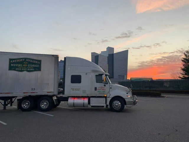 A semi truck is parked in a parking lot with a sunset in the background.