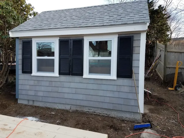 Completed outbuilding with shingle siding and shutters