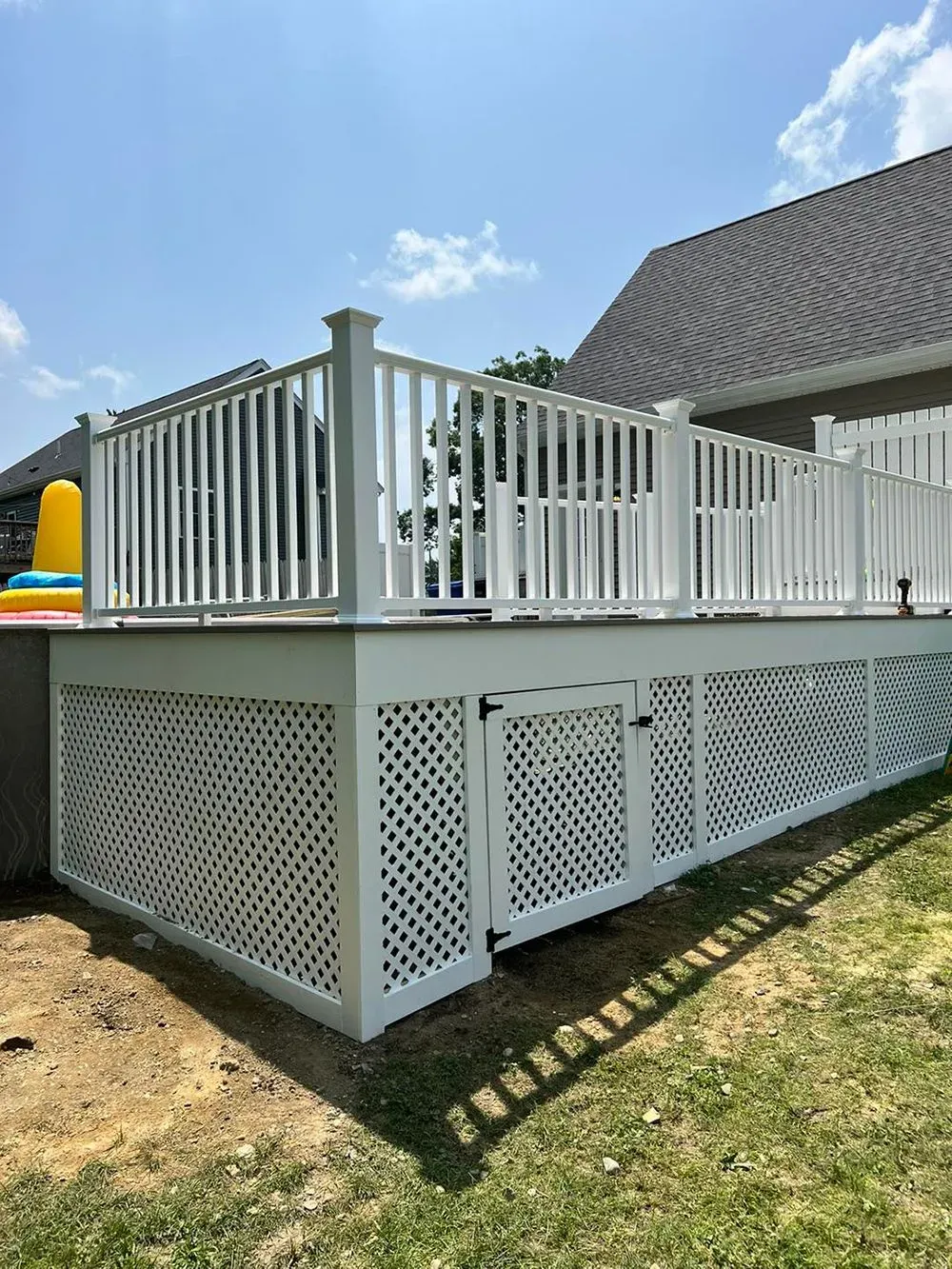 A white deck with a white railing and a fence in front of a house