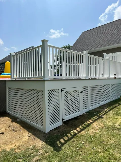 A white deck with a white railing and a fence in front of a house