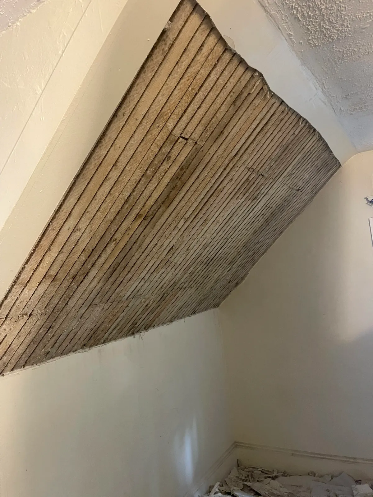 A partially removed wall ceiling with exposed wooden laths, indicating renovation or repair work in progress.