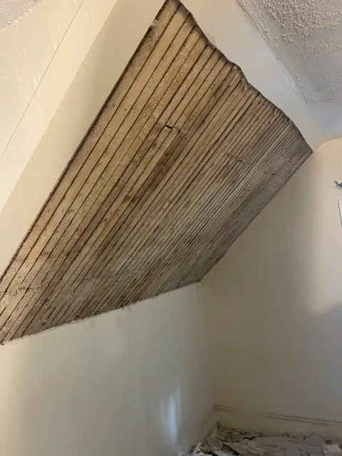 A partially removed wall ceiling with exposed wooden laths, indicating renovation or repair work in progress.