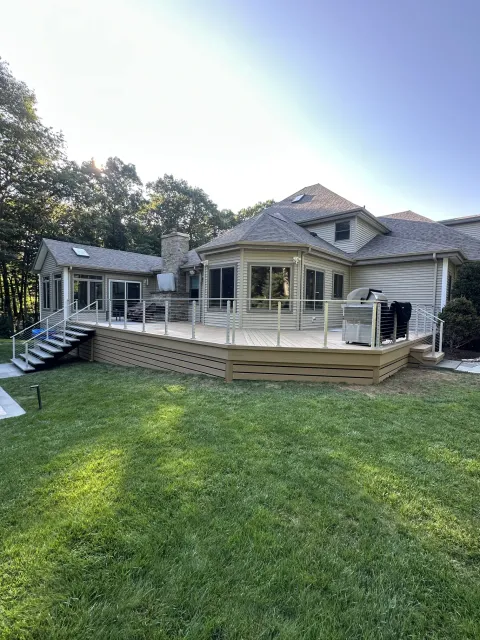 suburban-home-with-large-wraparound-deck-overlooking-green-lawn-and-wooded-backyard.webp