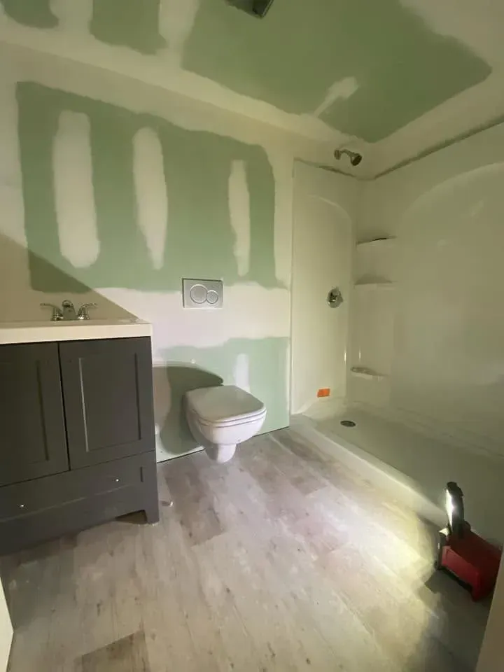 Partially renovated bathroom with green drywall patches, vanity, toilet, and tub under construction