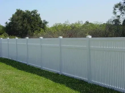 White vinyl fence along a grassy lawn with trees in the background