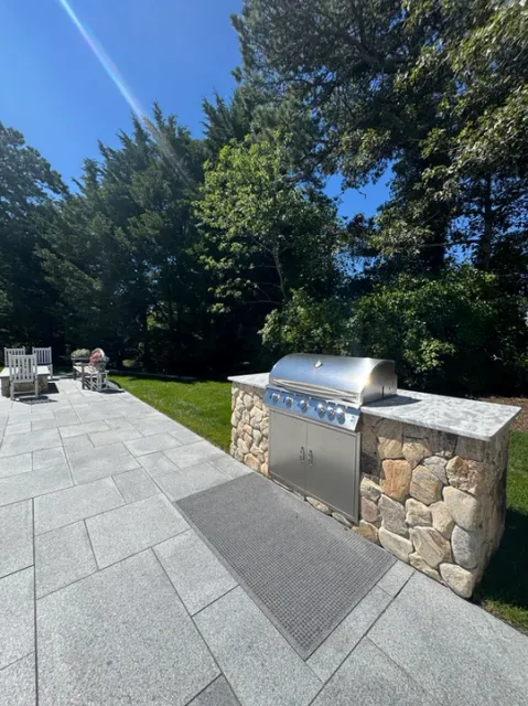 Outdoor kitchen with built-in stainless steel grill, concrete patio, green lawn.