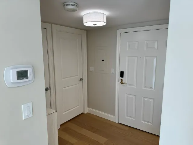 Bright hallway with white doors, wall thermostat, and ceiling light over wood floors.