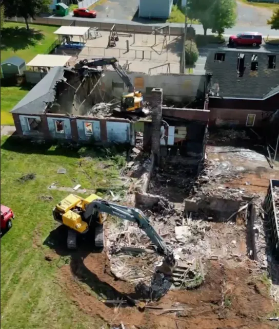 Aerial view of a demolition site with an excavator tearing down a burned brick building.