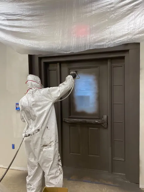 Painter spraying finish coat on a wood door