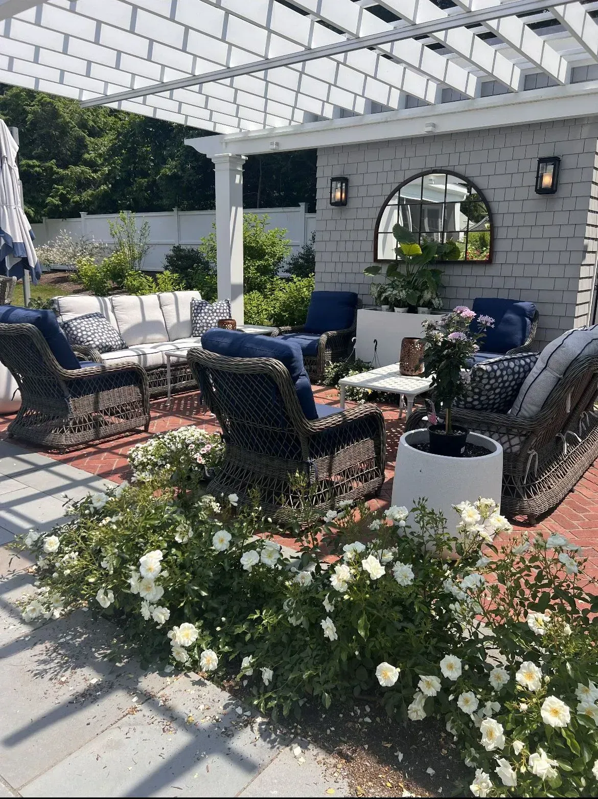 Patio seating area with black wicker chairs, blue cushions, white flowers, and a pergola overhead