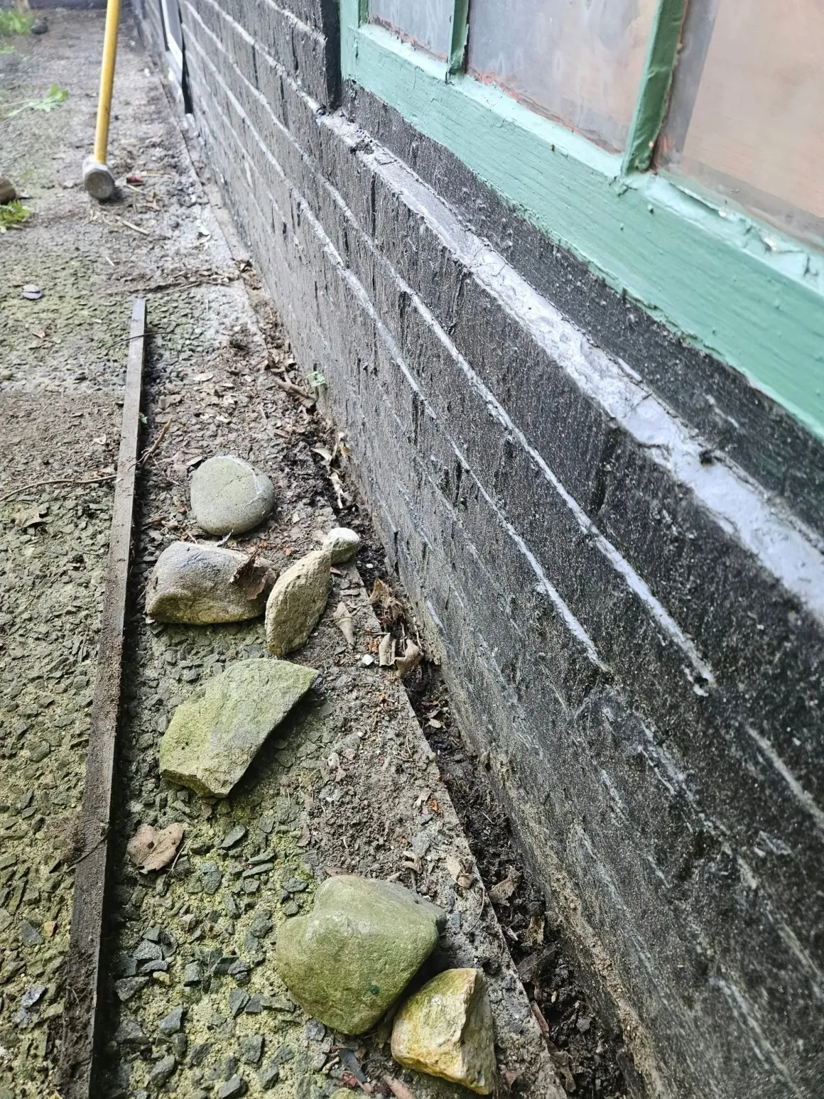 Cracked gravel walkway beside a building wall with stacked stones and green trim