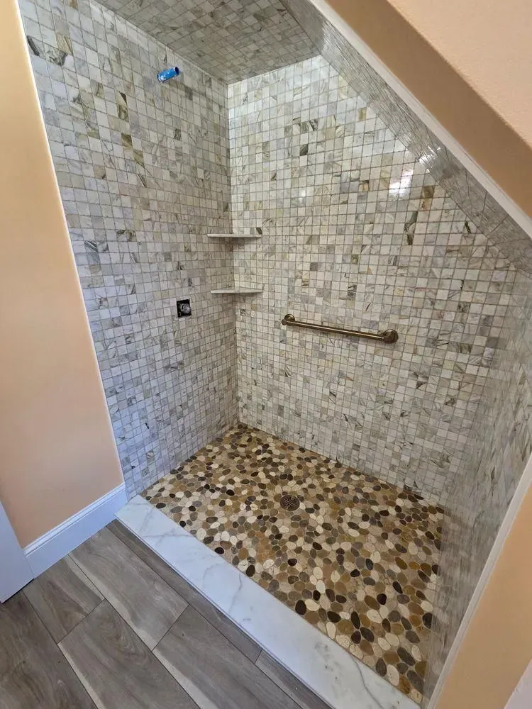 Tiled walk-in shower with mosaic floor, built-in shelf, and sloped ceiling.