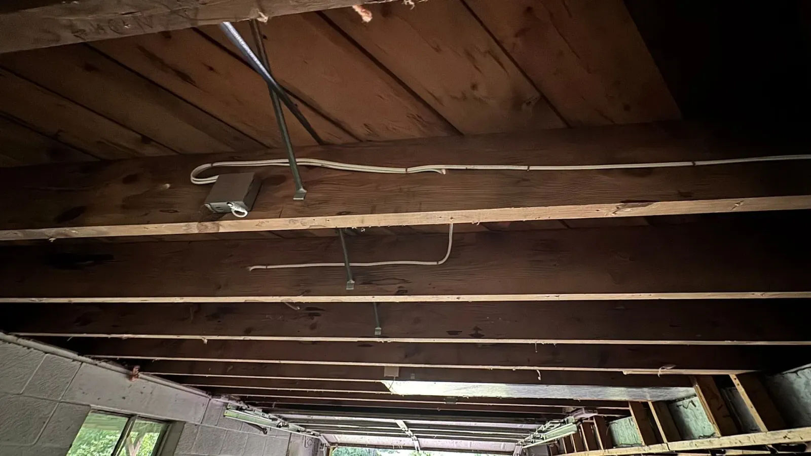 Wooden ceiling beams with electrical wiring, dark interior.