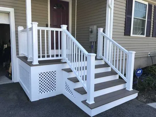 White railing and steps leading up to a house entrance with a burgundy door.