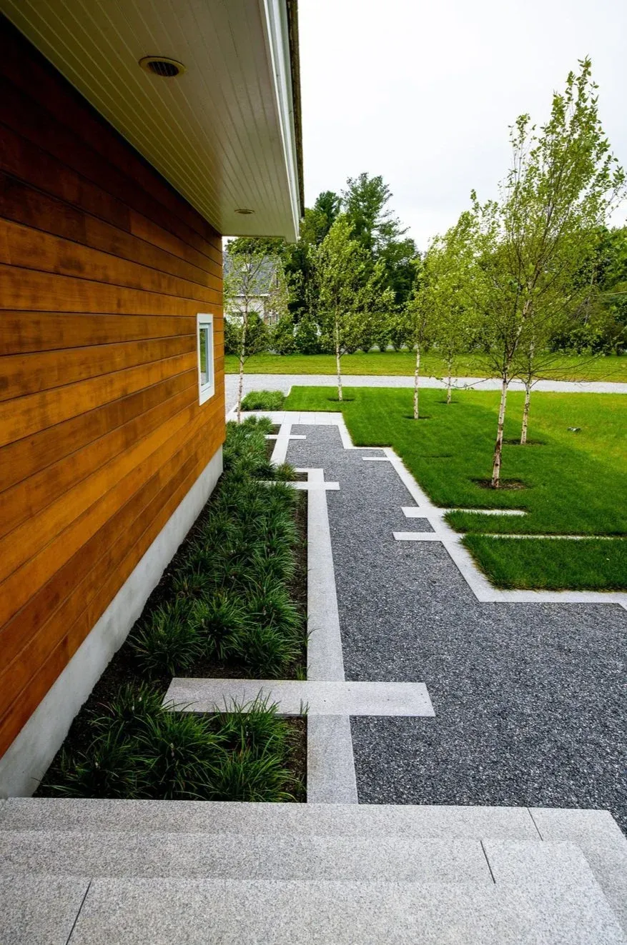 Modern front yard with a stone walkway, green grass, young trees, and a wooden house exterior.