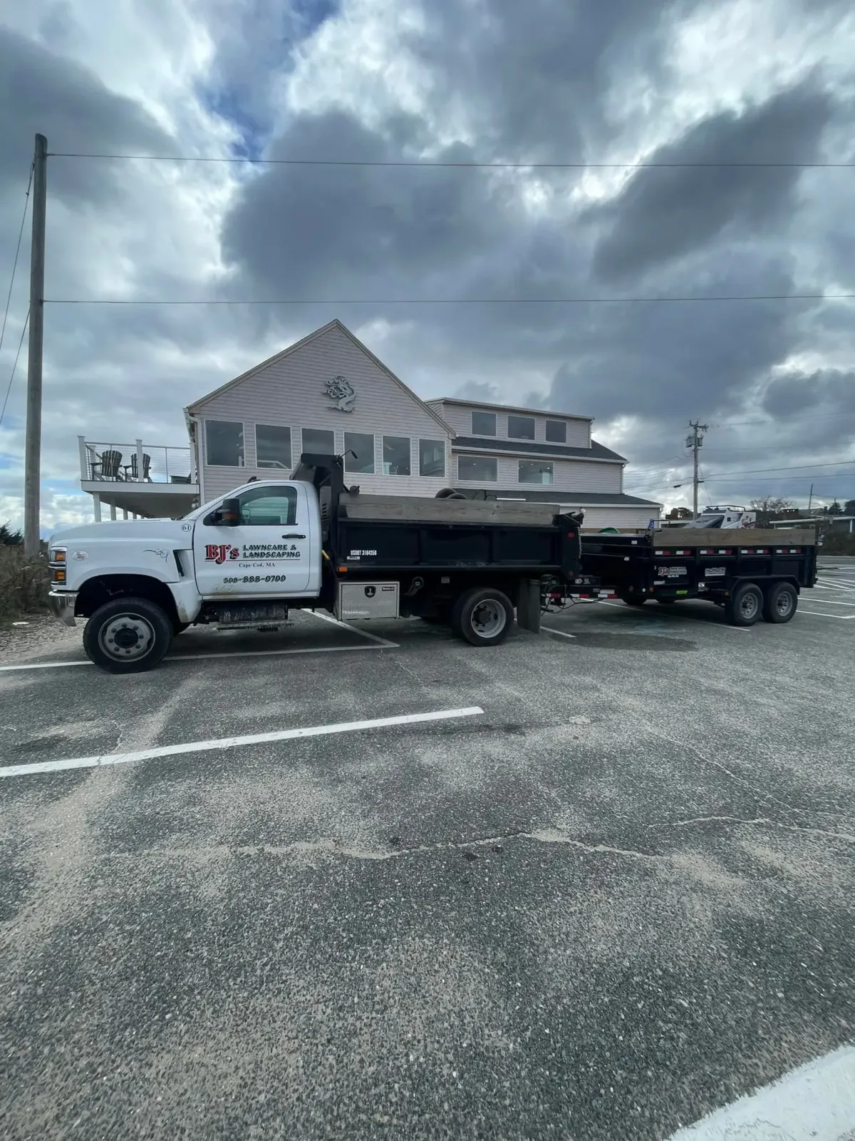 White dump truck with a trailer parked in front of a building under a cloudy sky.