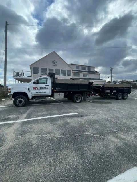 White dump truck with a trailer parked in front of a building under a cloudy sky.