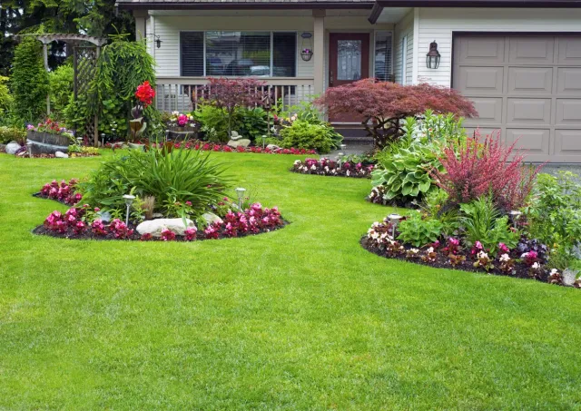 A front yard with a well-manicured lawn and two landscaped garden beds featuring colorful flowers and shrubs.