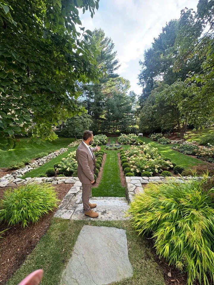 Formal gardens have a way of slowing you down, and this one is no exception.

Symmetrical flower beds, white hydrangeas in full form, and winding borders of natural stone give this Plymouth property a timeless, tucked-away feel. The central lawn walkway pulls your eye through the whole space, while layered greenery and tall trees create a sense of privacy that is hard to manufacture. This is what thoughtful landscape design looks like when every plant and path has a purpose.

As a landscaper, we love projects like this because they blend structure with softness. Our residential landscaping work covers everything from the initial design to plant installation, and irrigation system installation keeps gardens like this hydrated through the warm months without daily effort. Hardscape touches like stone paths and patio design services can bring the same sense of order to any backyard.

Early fall is a wonderful time to plan a garden transformation on the South Shore, since cooler days are ideal for planting and design work. If your outdoor space in Plymouth, Duxbury, or Kingston could use this kind of care, we would love to hear your ideas.

Send South Shore Green Inc. a message to schedule a consultation and start planning your own garden retreat.