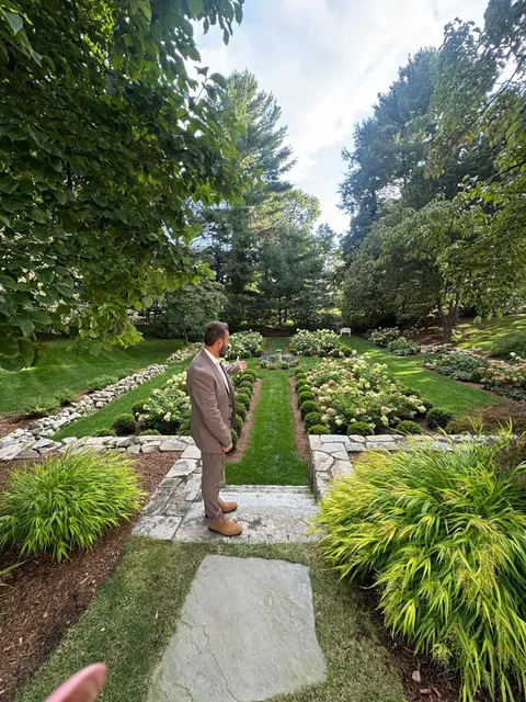 Formal gardens have a way of slowing you down, and this one is no exception.

Symmetrical flower beds, white hydrangeas in full form, and winding borders of natural stone give this Plymouth property a timeless, tucked-away feel. The central lawn walkway pulls your eye through the whole space, while layered greenery and tall trees create a sense of privacy that is hard to manufacture. This is what thoughtful landscape design looks like when every plant and path has a purpose.

As a landscaper, we love projects like this because they blend structure with softness. Our residential landscaping work covers everything from the initial design to plant installation, and irrigation system installation keeps gardens like this hydrated through the warm months without daily effort. Hardscape touches like stone paths and patio design services can bring the same sense of order to any backyard.

Early fall is a wonderful time to plan a garden transformation on the South Shore, since cooler days are ideal for planting and design work. If your outdoor space in Plymouth, Duxbury, or Kingston could use this kind of care, we would love to hear your ideas.

Send South Shore Green Inc. a message to schedule a consultation and start planning your own garden retreat.