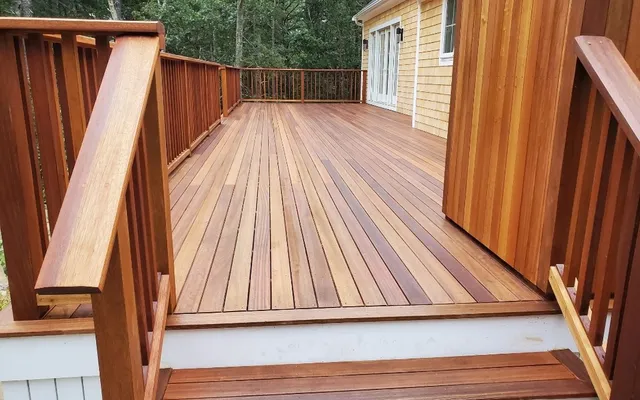 A newly built mahogany deck with matching rail and stairs beside a shingled house
