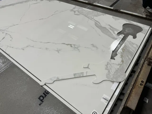 White marble tile with gray veining and two puzzle piece-shaped samples on top.