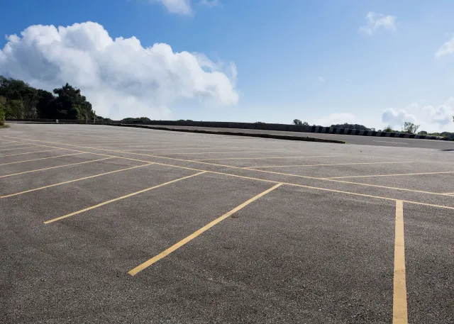 An empty parking lot with marked yellow spaces under a bright blue sky with scattered clouds.