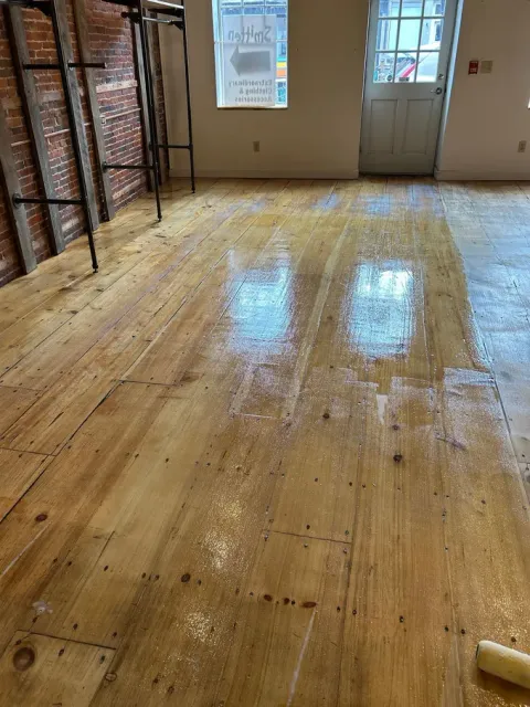 Wooden floor in a room with stacked boxes along the left wall and a door at the back.