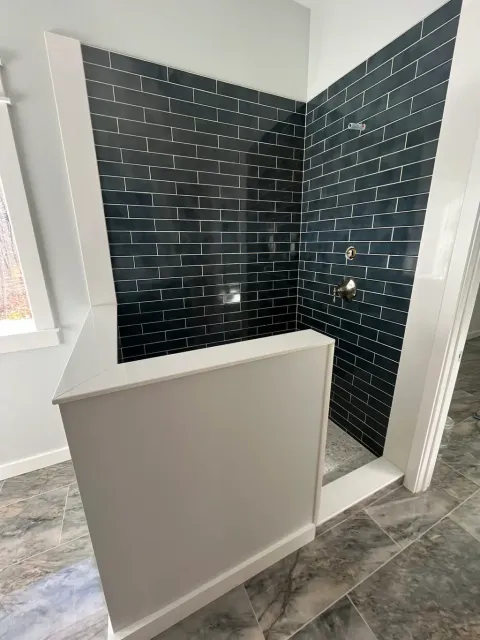 Walk-in shower in glossy navy subway tile behind a capped half wall