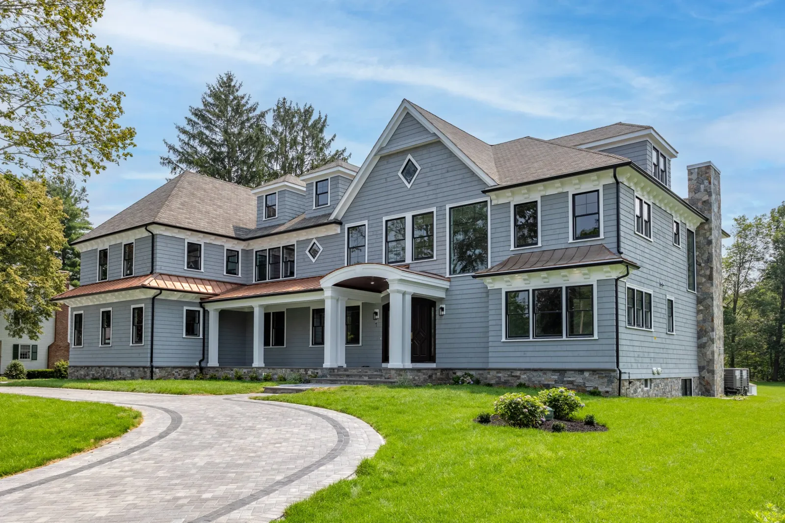 A large, modern house with gray siding and multiple windows, situated on a green lawn with a curved stone pathway leading to the front entrance.
