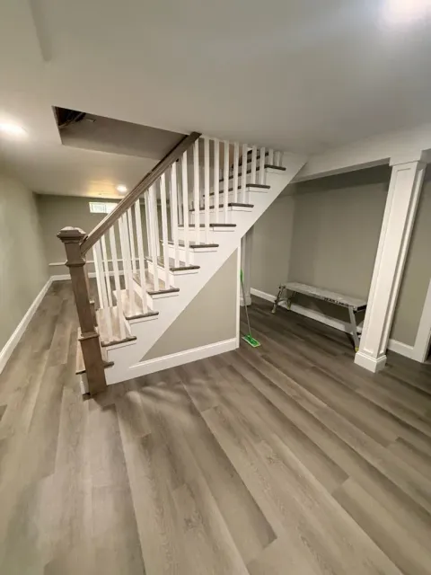 Interior staircase with white railings, wood floor, and a small bench under the stairs.