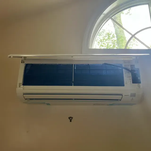 White air conditioning unit mounted on a beige wall under a rounded window.
