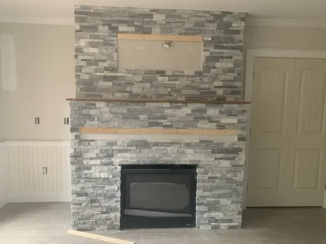 Living room stone fireplace with mantel and TV mount, flanked by white built-in cabinets and a closed door