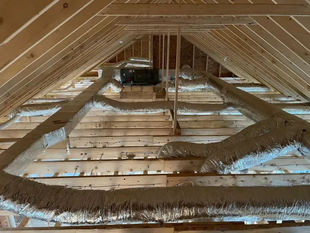 Attic with exposed wooden rafters and insulation batts lining the floor and edges