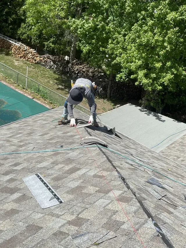 Person repairing a roof, surrounded by shingles and tools.