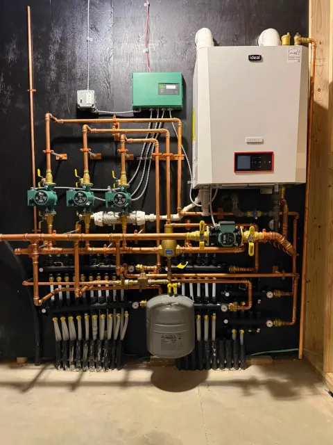Indoor utility wall with plumbing, pipes, valves, two boilers, and a water tank for a heating system