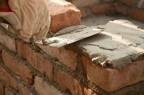 Gloved hands spreading mortar on a brick wall during masonry work