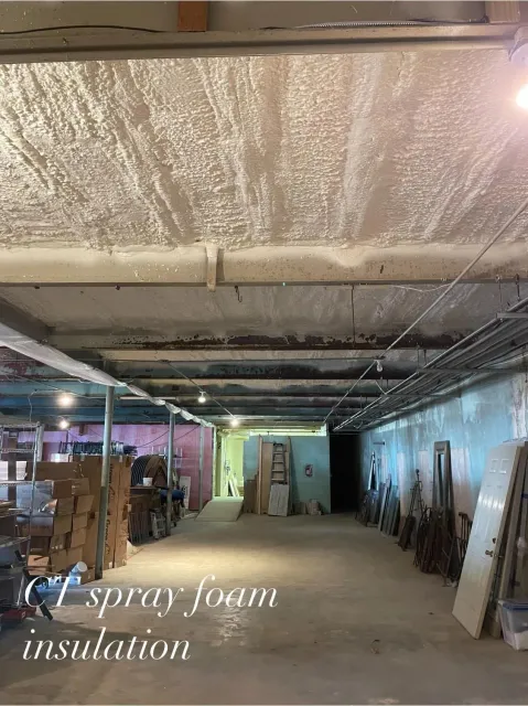 Warehouse interior with spray foam insulation on the ceiling; various objects line the walls.